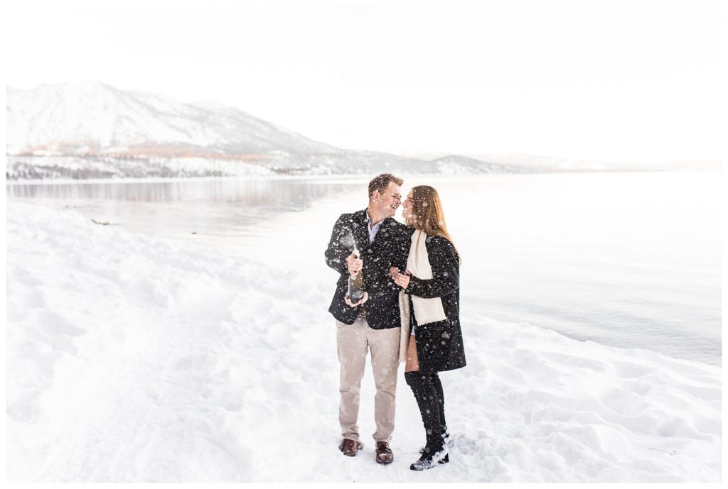 man and woman popping champagne in snowy lake tahoe