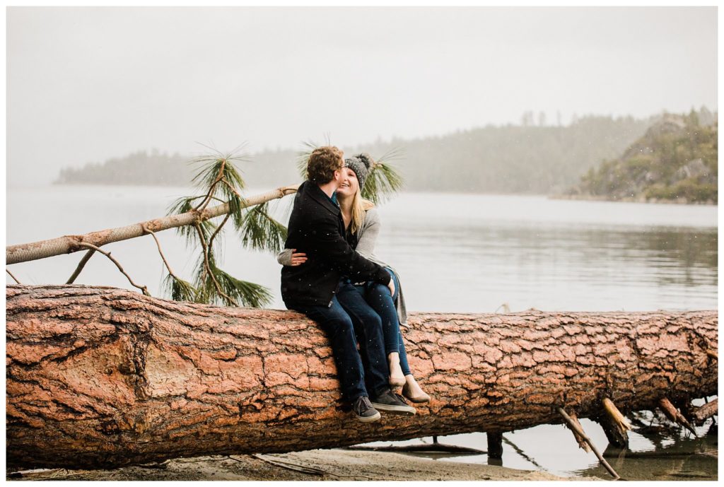 couple snuggling on tree stump by lake