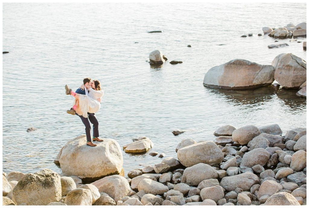 man lifting woman on rocks at sand harbor