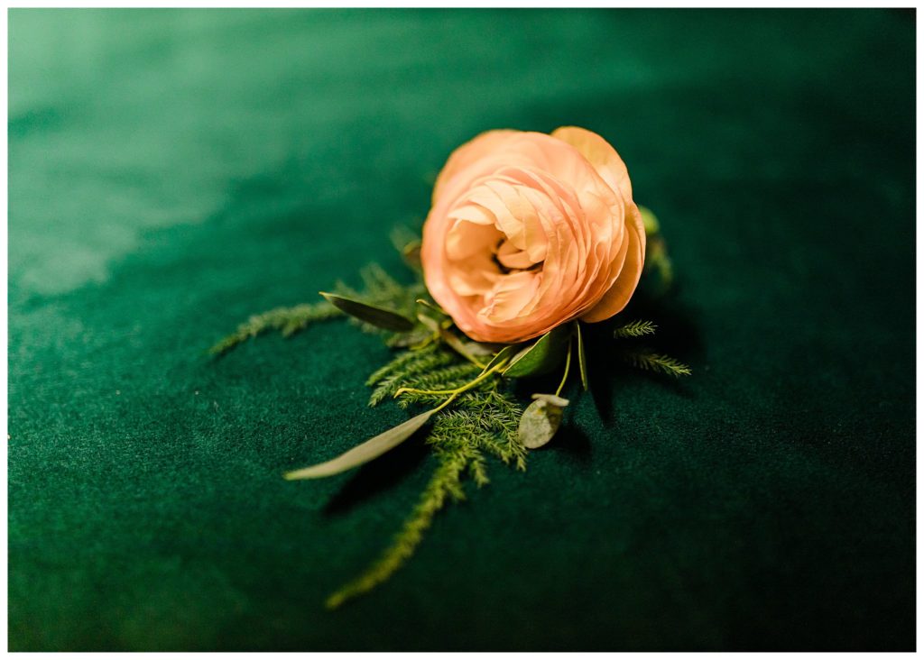 coral rose boutonnière on green velvet couch