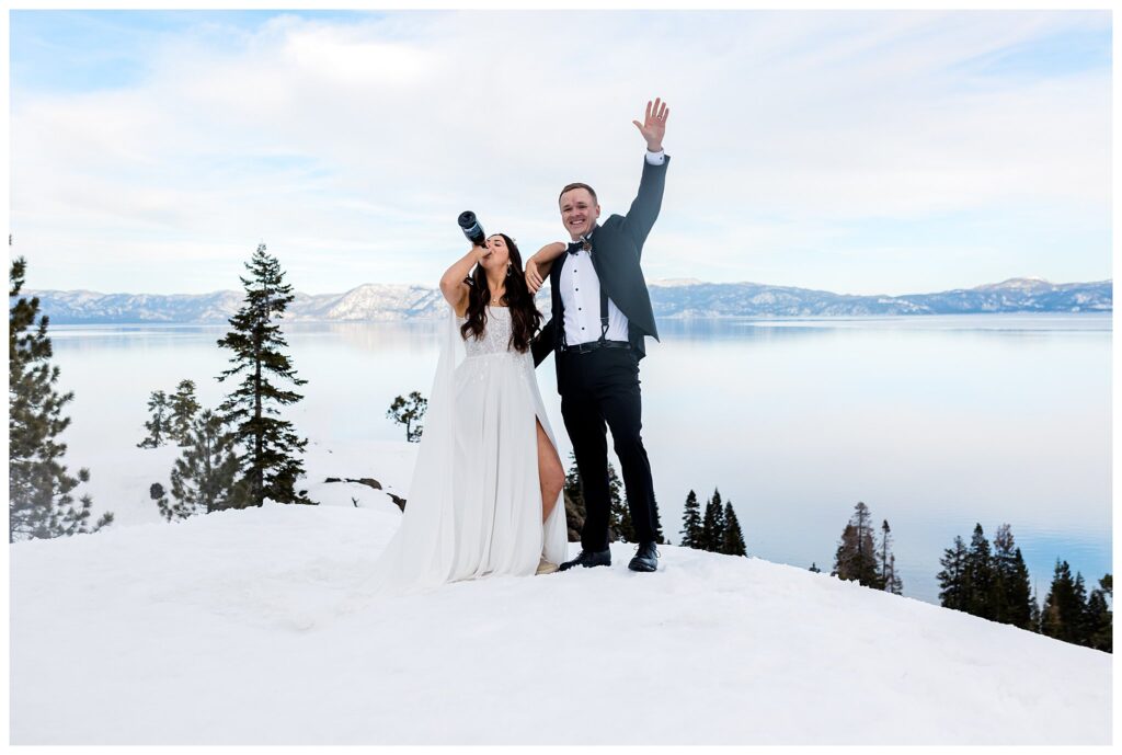bride swigging champagne while groom cheers her on for wedding photos in snow at lake tahoe