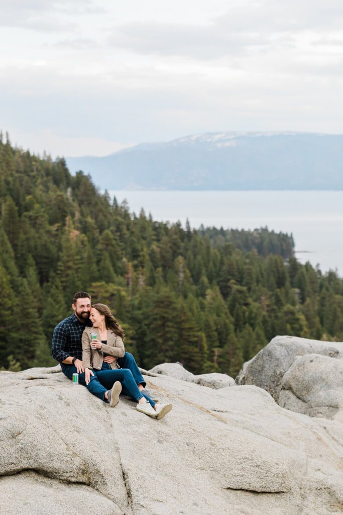 A couple sits on top of a rock overlooking lake tahoe.