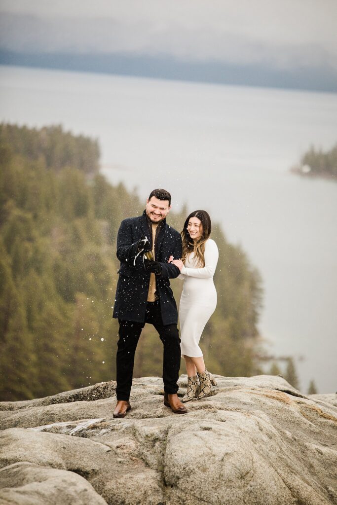 Lake Tahoe engagement photographer captures couple on top of a rock celebrating with a bottle of champagne.