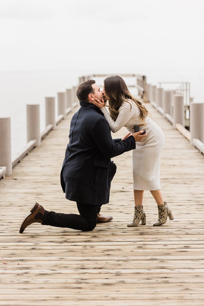 An engaged couple kissing on a dock.