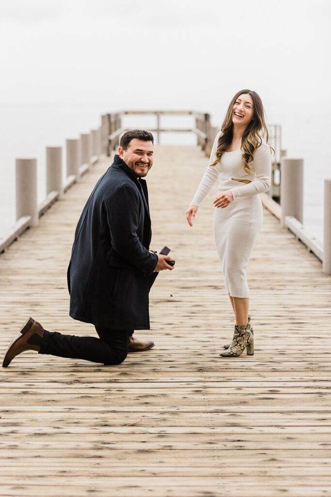 A man kneeling on a dock while proposing to a woman.