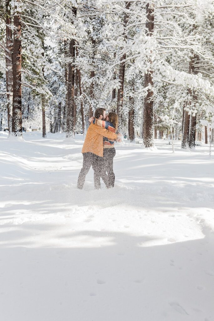 Two people hugging in the snow in a wooded area near Lake Tahoe.
