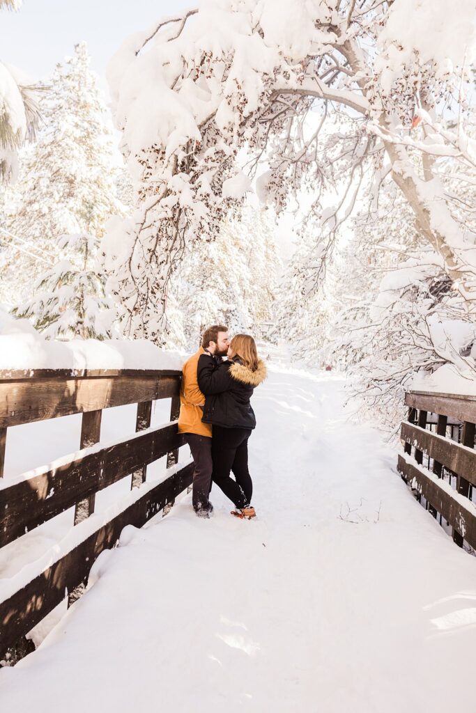 A couple embracing on a snowy wooden bridge near Lake Tahoe.