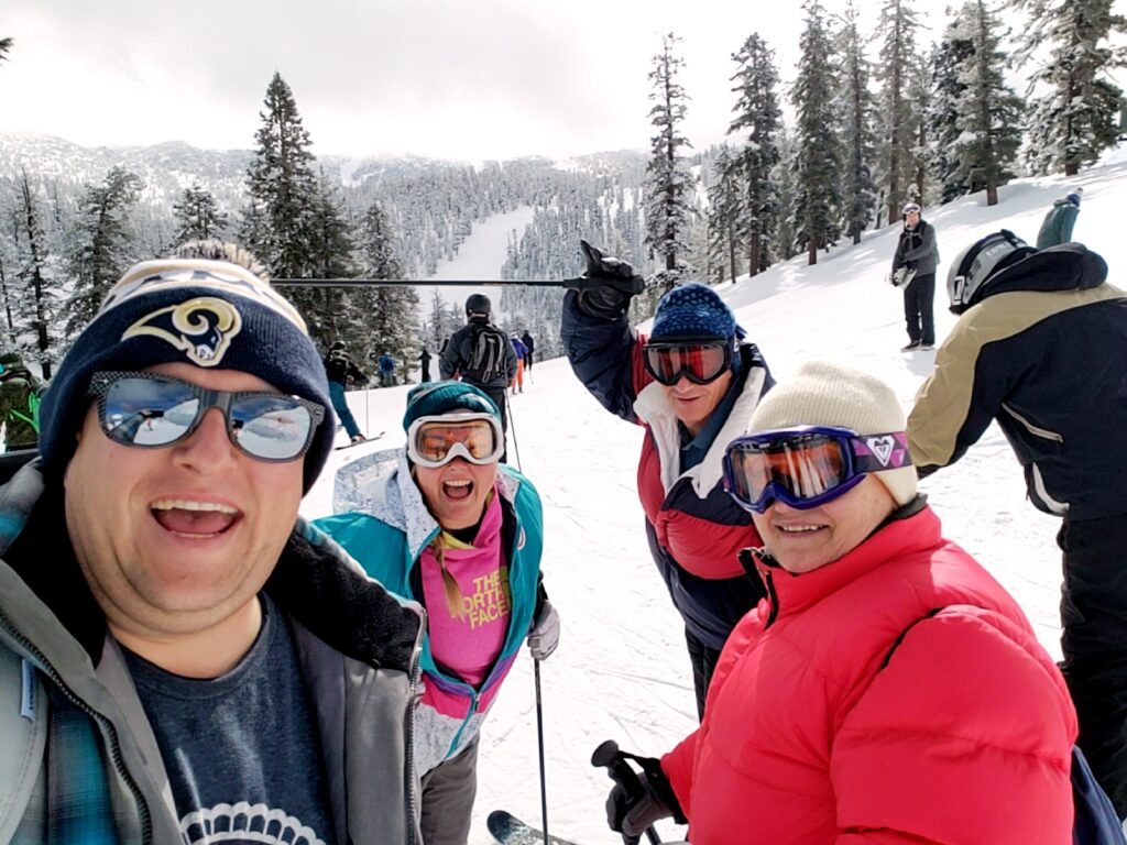 A group of people in winter gear pose for a selfie on a snowy ski slope with pine trees and mountains in the background, capturing one of the best things to do in Lake Tahoe.