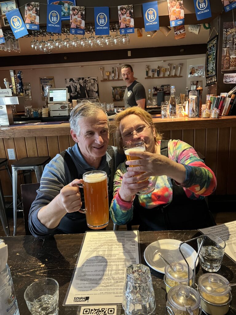 A man and woman sit together at a bar near Lake Tahoe, holding large glasses of beer and smiling as they discover the local charm.