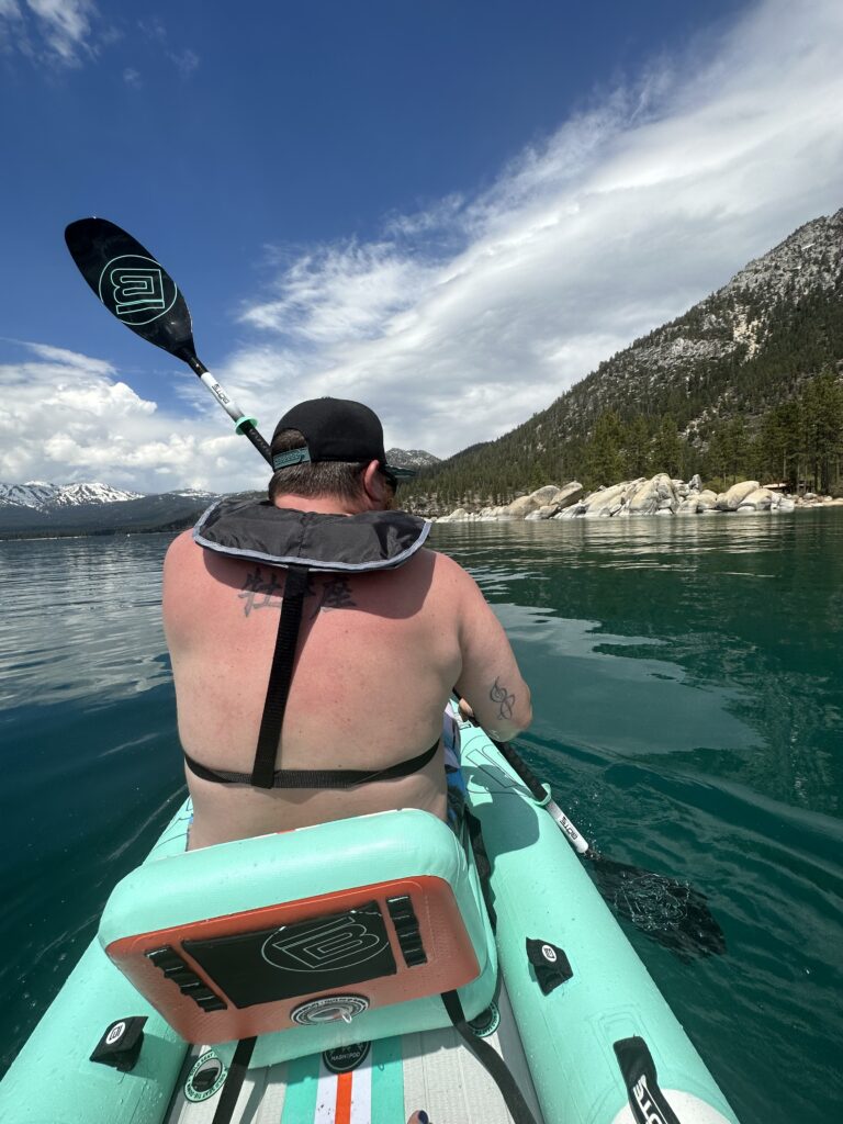 Discover Lake Tahoe as you kayak on clear turquoise waters, surrounded by tree-covered mountains and rocks under a partly cloudy sky. Experience one of the most breathtaking things to do in Lake Tahoe, offering unforgettable views and serene adventure.