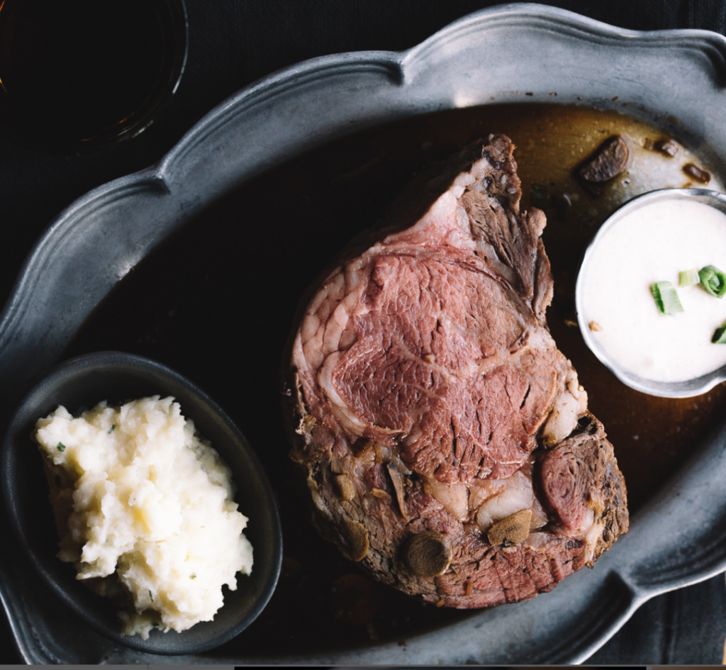 A serving of prime rib on a plate with a side of mashed potatoes and a cup of creamy sauce, perfect after exploring things to do in Lake Tahoe.