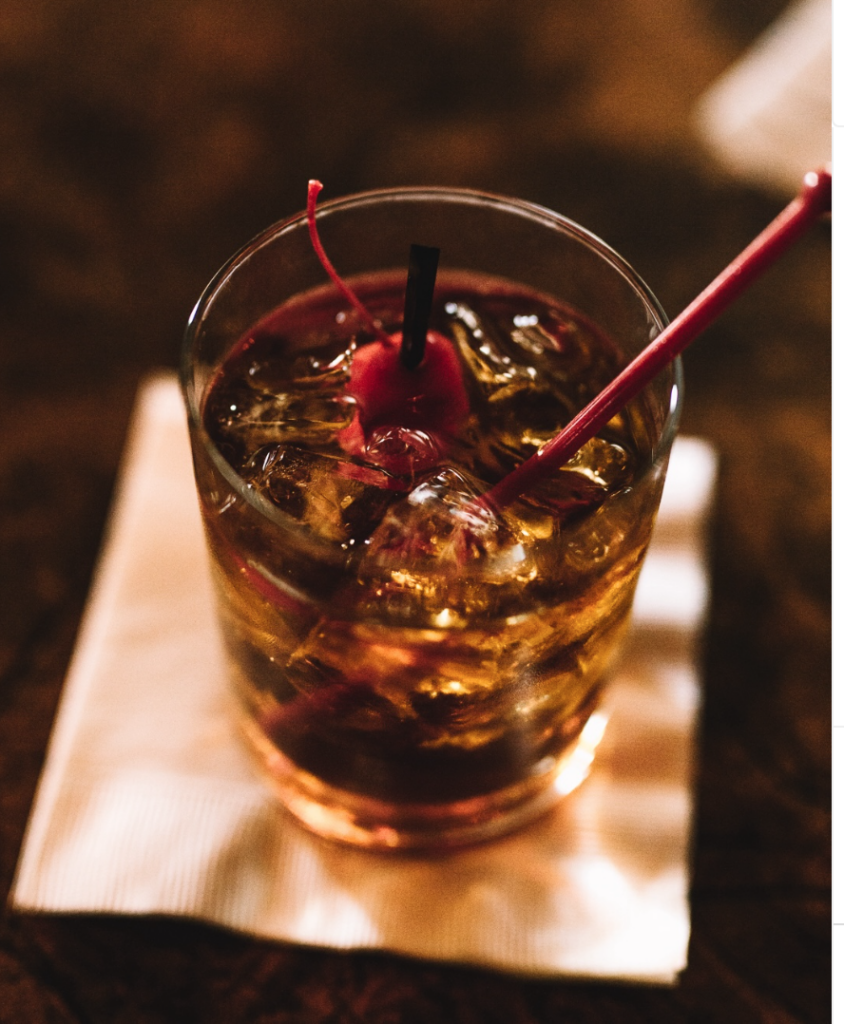 A cocktail with ice, a cherry, and a stir stick in a glass, placed on a white napkin—perfect for unwinding after you discover Lake Tahoe's natural beauty.