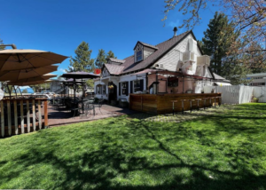 Discover Lake Tahoe at a sunny outdoor restaurant featuring patio seating, umbrellas, and a lush lawn. This charming spot boasts a classic design with a peaked roof and white siding, making it an ideal destination when exploring things to do in Lake Tahoe.