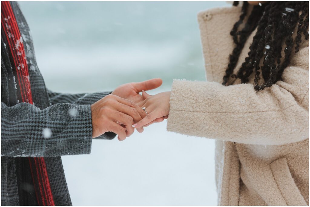 Two people holding hands outdoors in the snow, with one person wearing an engagement ring.